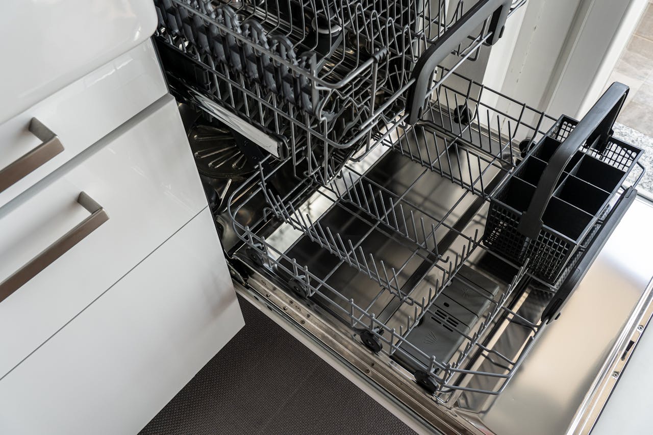 services-01 A clean and empty stainless steel dishwasher open in a modern kitchen setting.