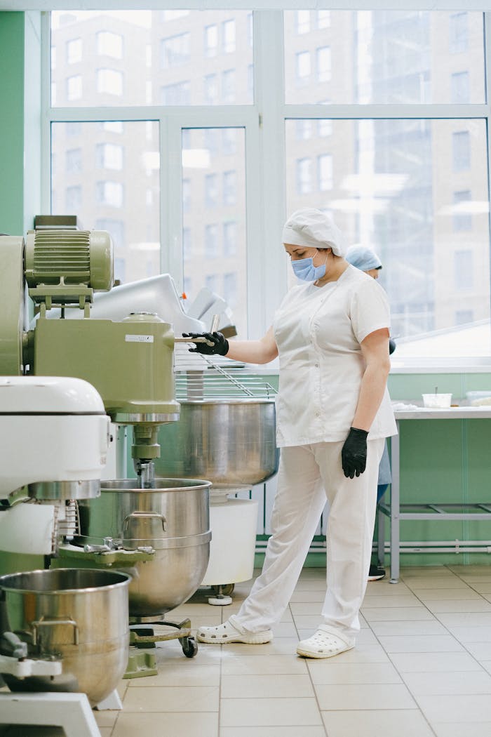 A food industry worker in a modern kitchen using an industrial mixer with protective gear.