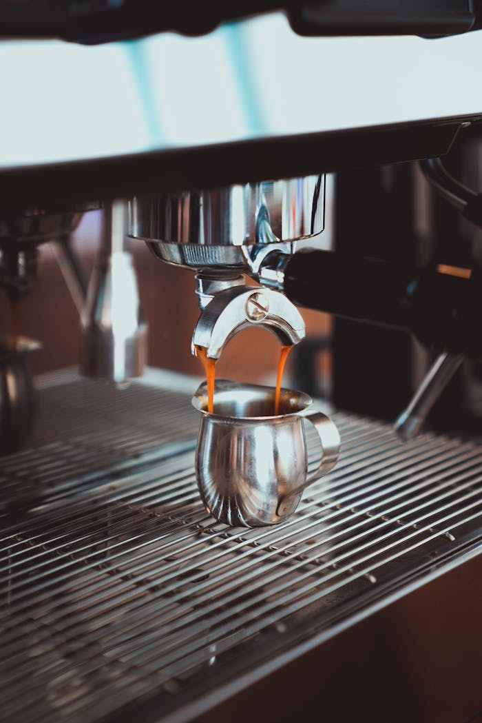 Close-up of espresso pouring from a coffee machine into a stainless steel cup.